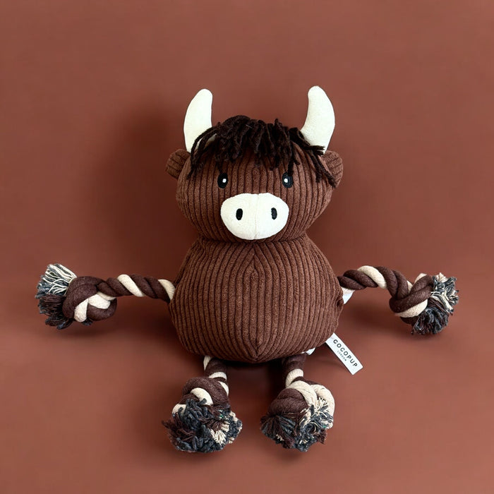 Brown corduroy dog toy shaped like a highland cow, with rope limbs, white horns, and snout.