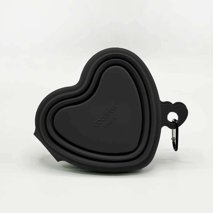 Black collapsible dog bowl with white heart pattern and a metal carabiner attached to the rim.