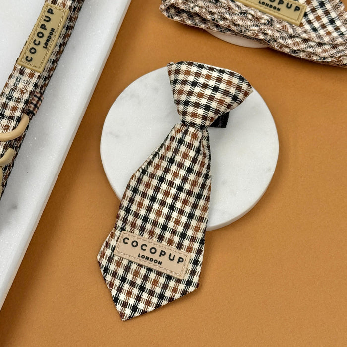 Brown and beige heritage check dog tie by Cocopup London displayed on a marble surface.
