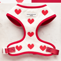 Knitted adjustable neck harness with red trim and heart pattern by Cocopup London, displayed on a marble surface.