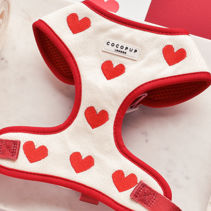 Cream knitted dog harness with red hearts and trim by Cocopup London, displayed on a marble surface.