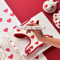 Hand holding a red knitted dog collar from Cocopup London with a pattern of small hearts.