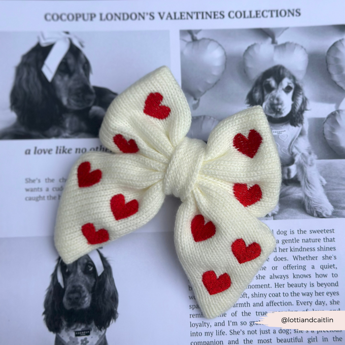 White knit bow tie with red hearts, displayed on a magazine featuring a festive dog and balloons.