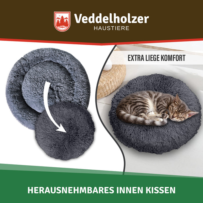 Rundes Innenkissen wird aus dem Bettring gehoben, daneben schläft eine getigerte Katze eingerollt im dunkelgrauen Bett