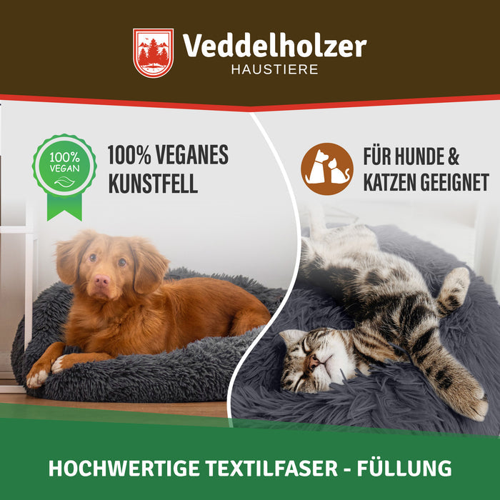Brauner Retriever im dunkelgrauen Bett, daneben eine getigerte Katze auf dem Rücken – Siegel „100 % veganes Kunstfell“