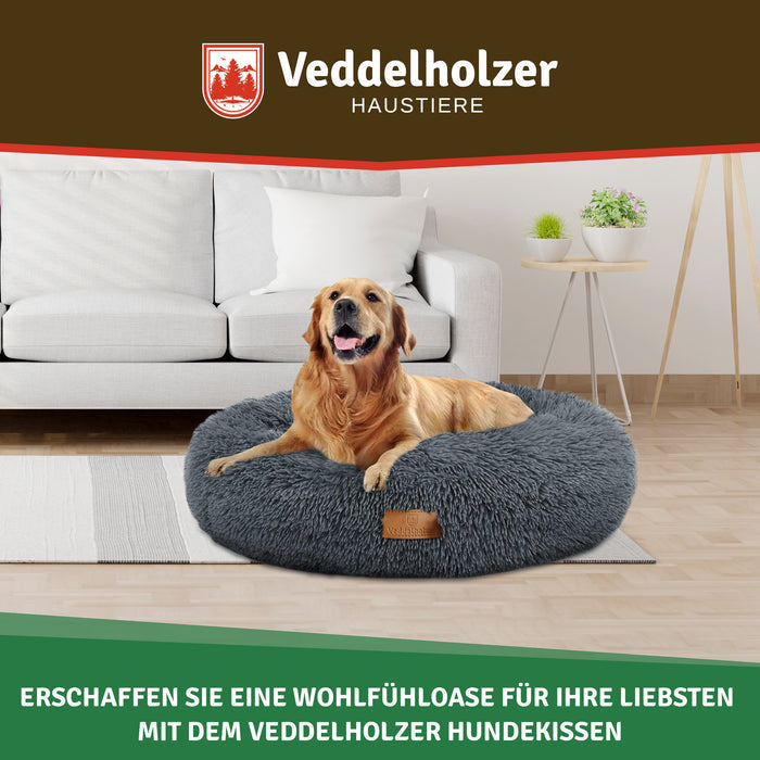 Golden Retriever ruht im dunkelgrauen Plüschbett auf dem Wohnzimmerteppich vor einem weißen Sofa