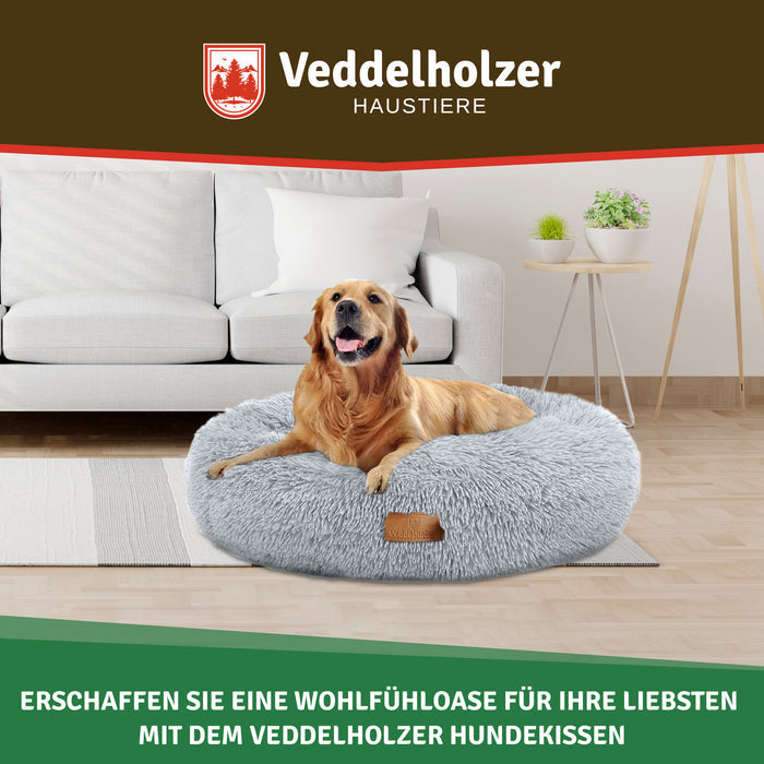 Golden Retriever entspannt im hellgrauen Plüschbett vor einem weißen Sofa im hellen Wohnzimmer