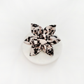 Ivory tortoiseshell-patterned fabric dog collar flower by Cocopup London displayed on a round white surface.