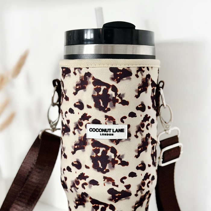 Ivory tortoiseshell Cocopup London tumbler carry case with Stanley Quencher 40oz, black lid, straw, and brown strap.