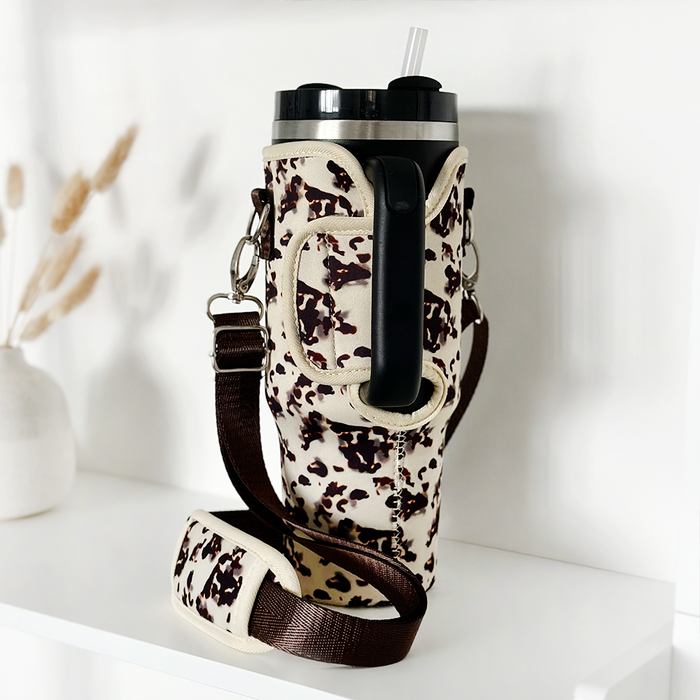 Stanley Quencher 40oz with black lid in an ivory tortoise-patterned Cocopup tumbler case on a white shelf.