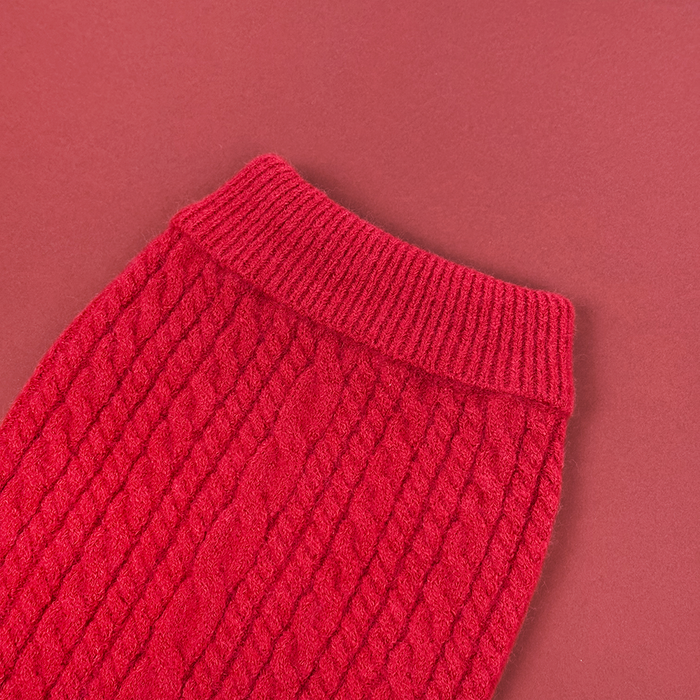 Close-up of a red cable knit jumper sleeve in mulled wine shade on a matching background.