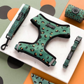 A Cocopup London Khaki Leopard Adjustable Neck Harness, Lead & Collar Bundle is beautifully displayed on a marble surface. This set includes a harness, leash, waste bag dispenser, and collar. The backdrop showcases orange and black circular patterns on green and grey surfaces.