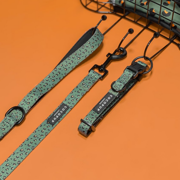A Khaki Leopard Adjustable Neck Harness, Lead & Collar Bundle from Cocopup London lies flat on an orange surface next to a black wire basket. This bundle features a pattern similar to leopard spots and includes a black tag with white text.