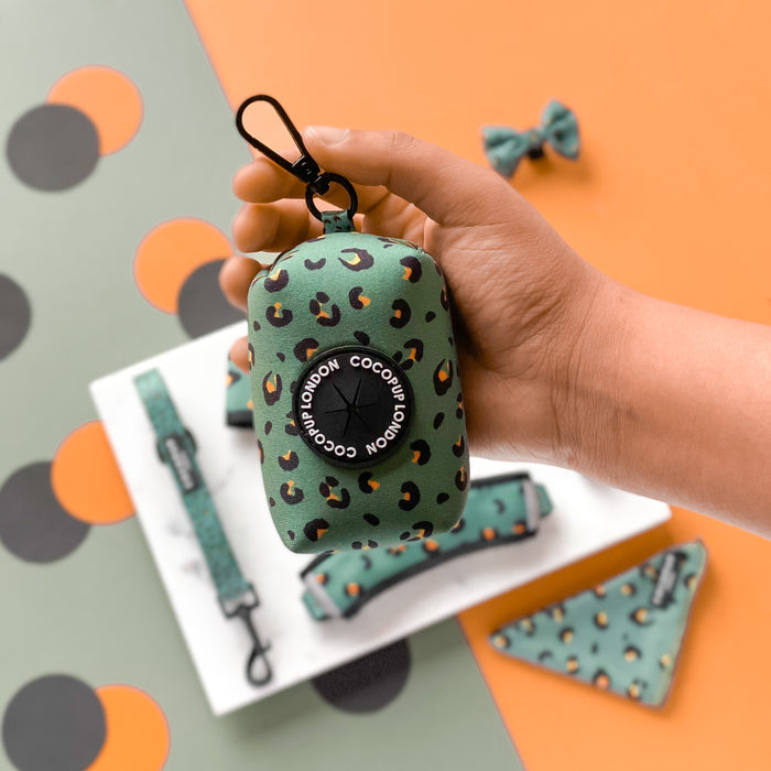 Hand holds a khaki leopard print Cocopup London poop bag holder; matching accessories sit in the background.