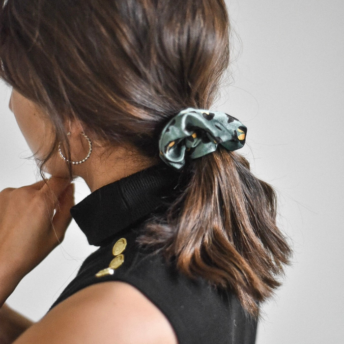 Woman with wavy brown hair in a ponytail wears a khaki leopard print scrunchie.
