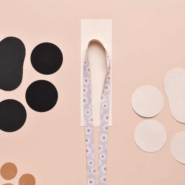 Daisy Chain lanyard with floral ribbon and colorful paper circles on a beige background.