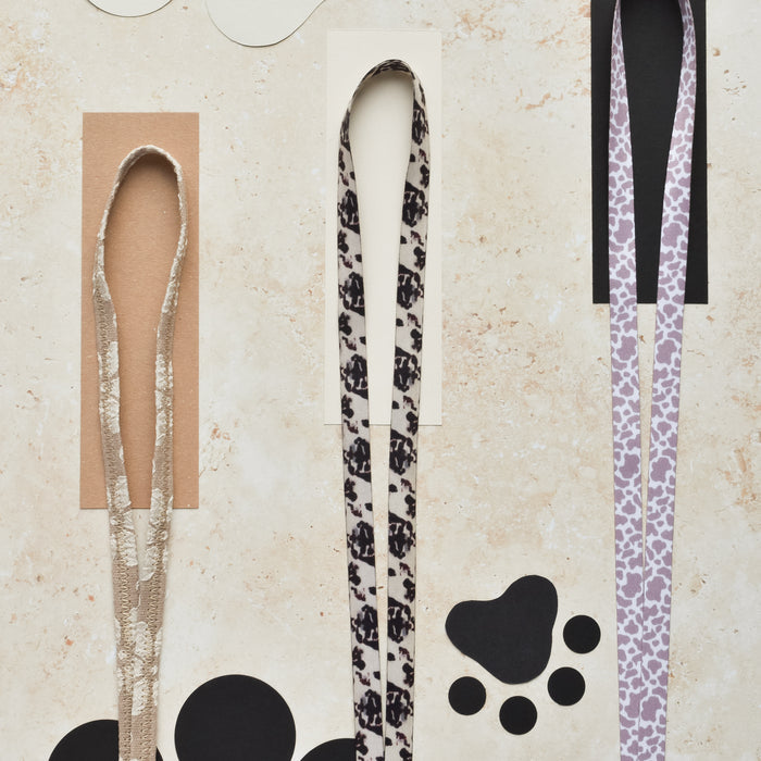 Ivory Tort lanyard by Cocopup London standing upright on a textured surface with paw print pattern.