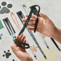 Hands hold a green patterned dog leash with whistle; a khaki leopard print Cocopup London lanyard lies nearby.