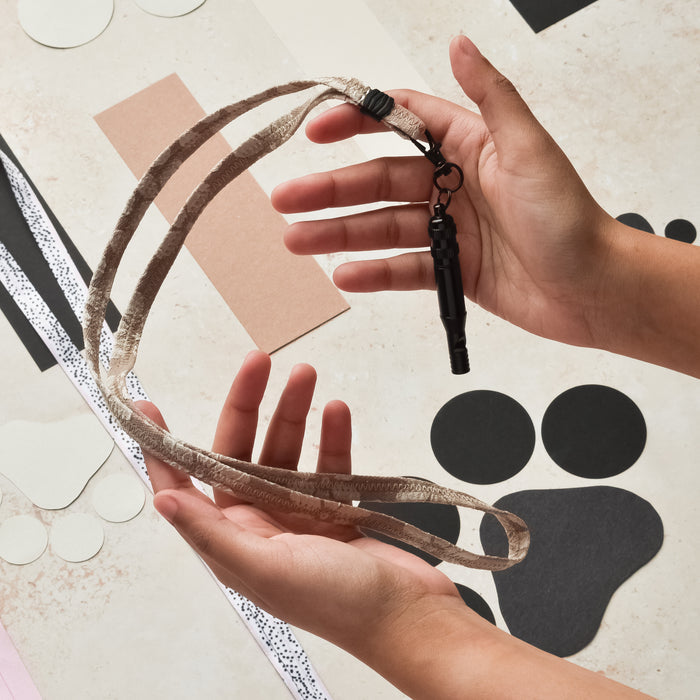 Hands holding a mocha floral Cocopup London lanyard with attached black whistle.
