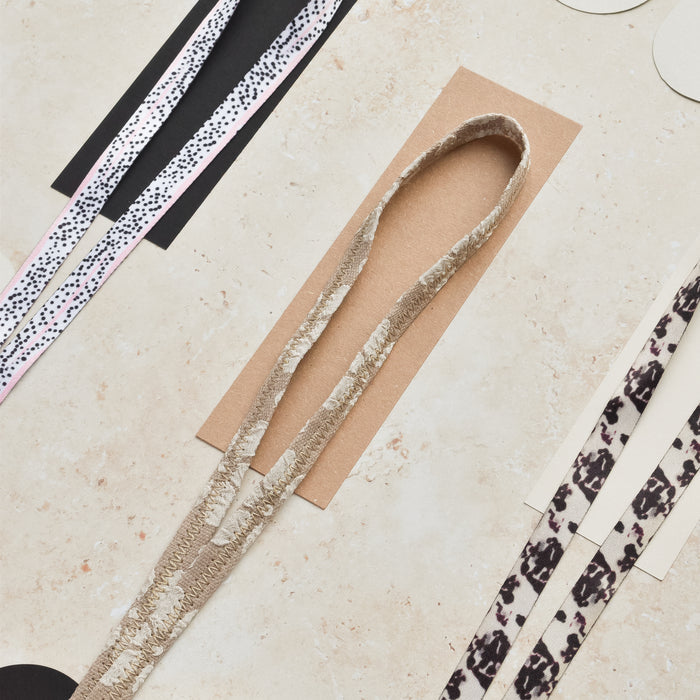 Cocopup London Mocha Flower lanyard with floral print, patterned ribbons, and papers on a light beige surface.