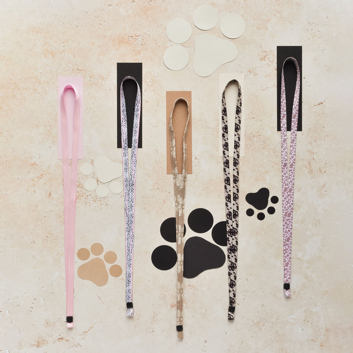 Five patterned fabric lanyards, including a brown floral design, arranged above paw print cutouts.