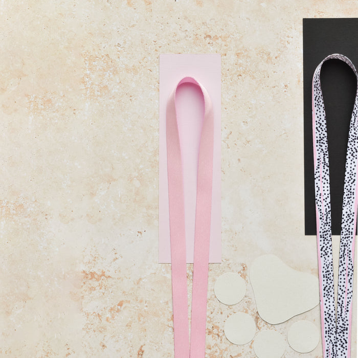 Baby pink Cocopup London lanyard rests on papers with a patterned ribbon, against a beige speckled background.