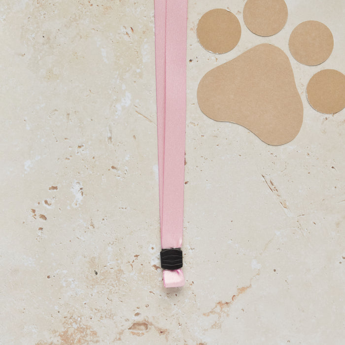 Pink Cocopup London lanyard with metal clip next to a brown paw print card on a light stone background.