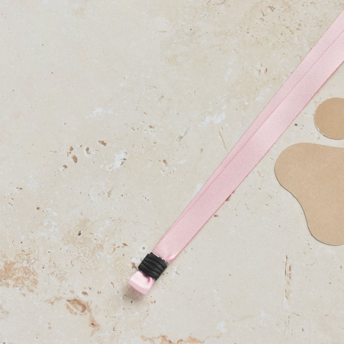 Baby pink Cocopup London lanyard next to a large paw print on a beige speckled surface.