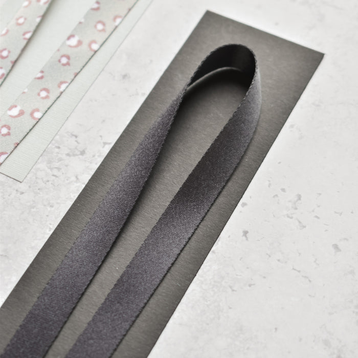 Plain black Cocopup London lanyard looped on a card beside patterned fabric strips on a light background.