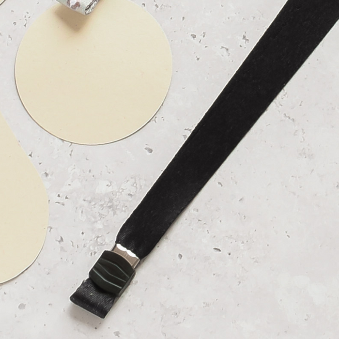 Plain black Cocopup London lanyard with silver clasp on a light textured surface, cream paper circles in background.