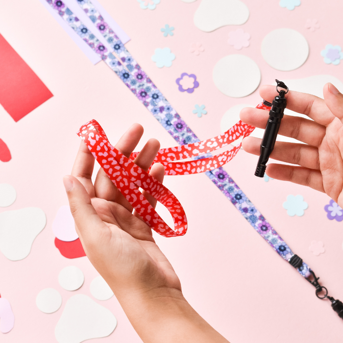 Hands hold a red and pink leopard print Cocopup London lanyard above craft supplies on a pink background.