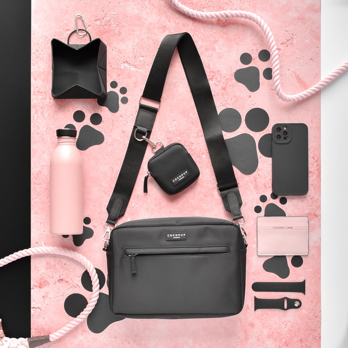 Black Cocopup London Large Dog Walking Bag with pink accessories, phone, and water bottle on a pink background.
