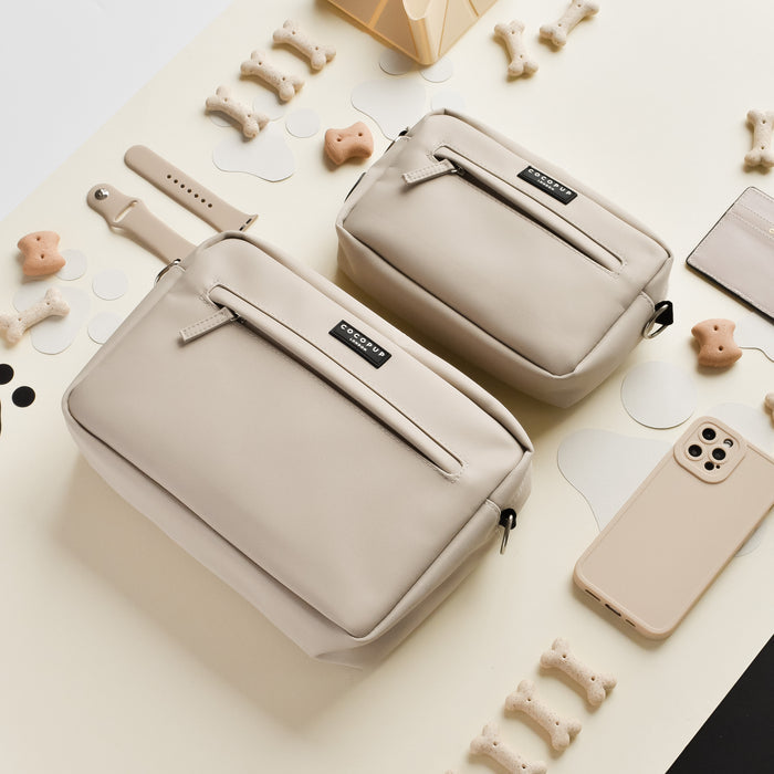 Two caramel brown dog walking bags on a cream surface, shown with assorted accessories and dog treats.