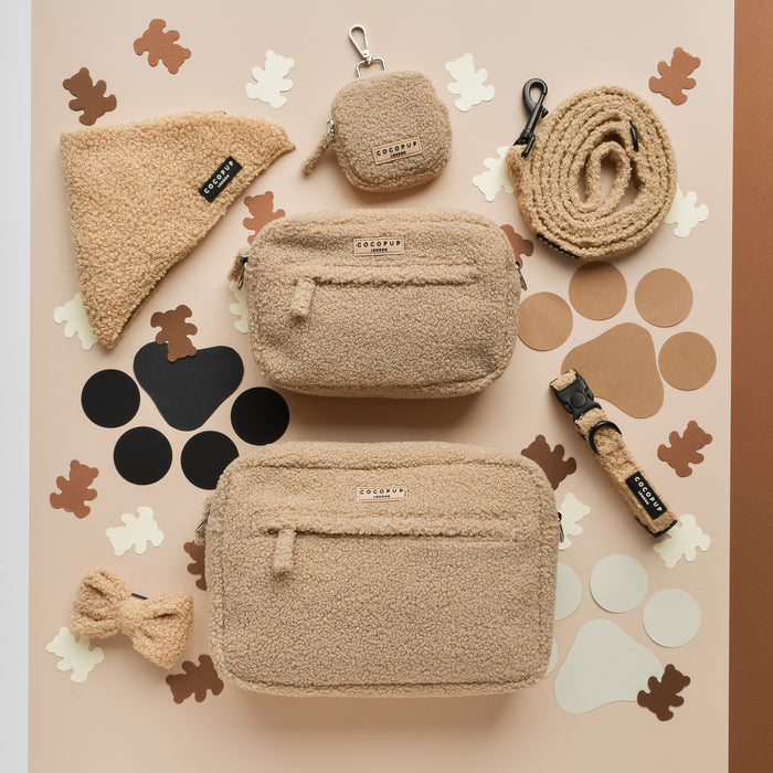 Large tan sherpa dog walking bag with matching leash, collar, and bow tie on a paw-print background.