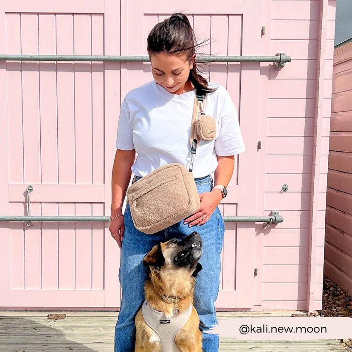 Woman in a white shirt and jeans by a pink wall holds a Cocopup London large teddy-texture beige dog walking bag.