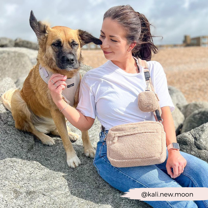 Woman in a white shirt on beach rocks with her brown dog and a beige Cocopup London dog walking bag.