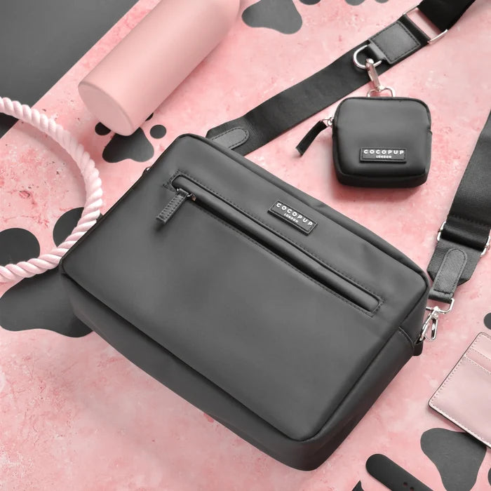Large black Cocopup London dog walking bag with matching treat pouch on a pink surface with black spots.