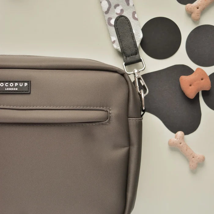 Sage leopard Cocopup London dog walking bag with black zipper, shown on a light surface beside dog bone treats.