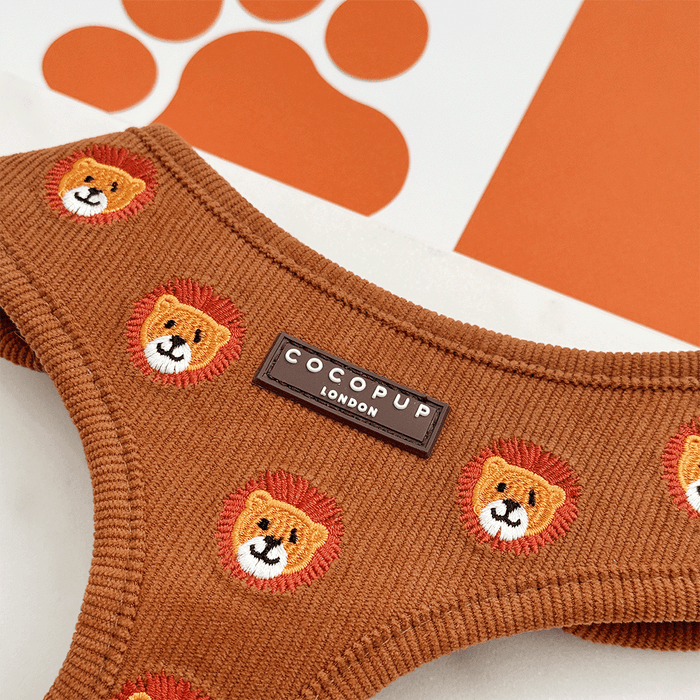 A brown / orange corduroy dog harness with embroidered lion faces.