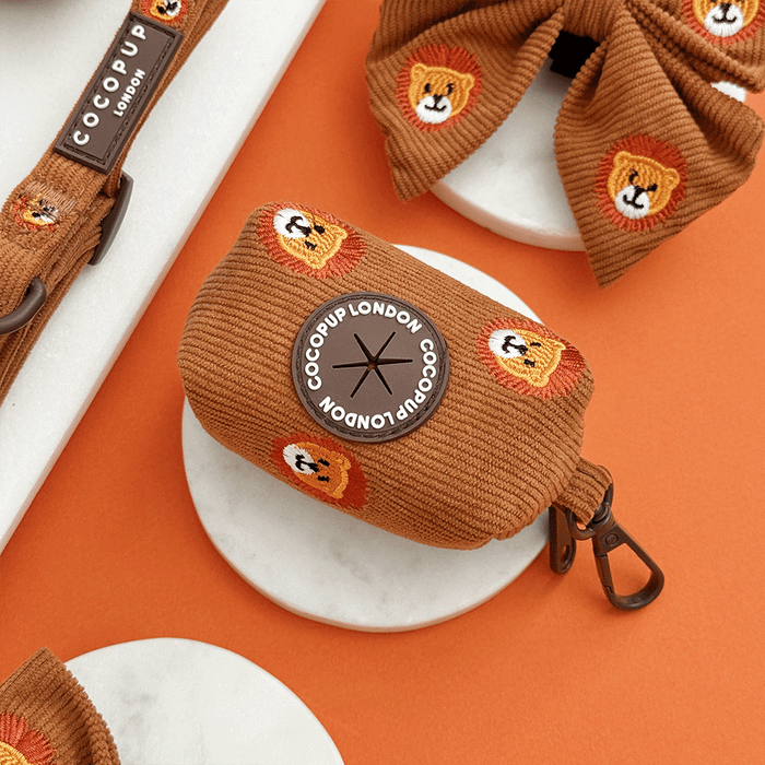 A brown / orange corduroy poop bag holder, to hold dog poo bags, with embroidered lion faces. With brown hardware.