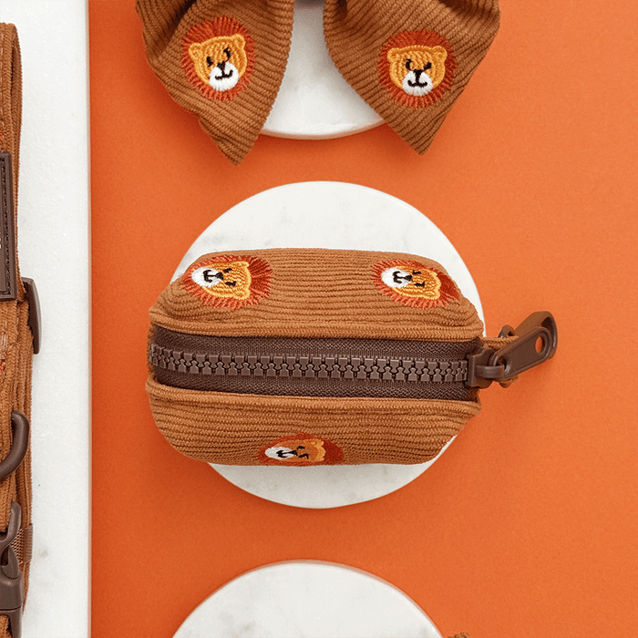 A brown / orange corduroy poop bag holder, to hold dog poo bags, with embroidered lion faces. With brown hardware.