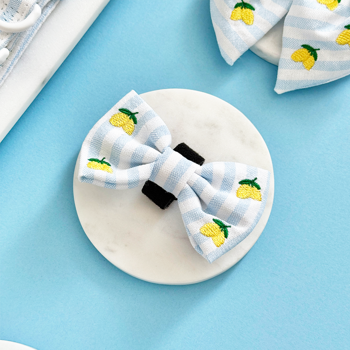 Blue and white striped bow tie with embroidered lemons, displayed on a marble surface.