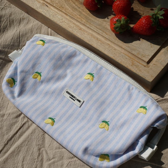 Blue and white striped makeup bag with lemon embroidery, shown next to fresh strawberries.