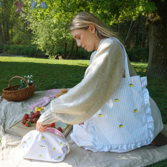 Woman picnicking on a blanket with a yellow lemon-patterned Cocopup London tote bag beside her.