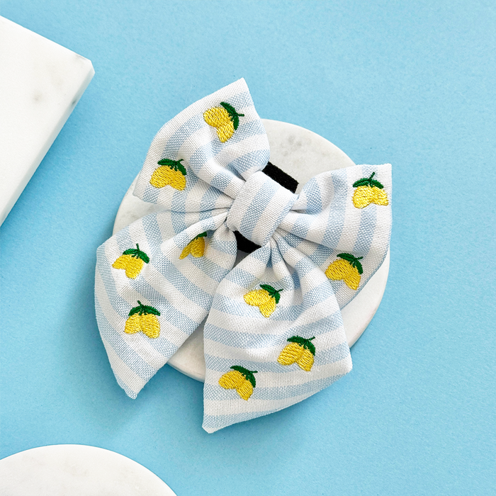 Yellow lemon print sailor bow tie by Cocopup London on a round surface, set against a light blue background.
