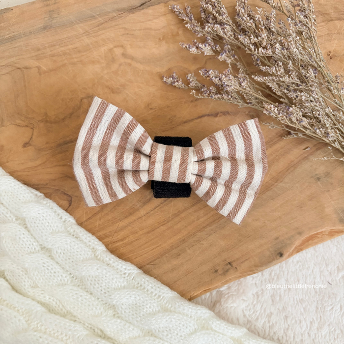 Brown and white striped linen bow tie with black center, displayed on wood beside dried flowers.