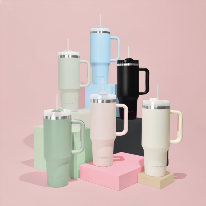Six milky coconut-colored stainless steel tumblers arranged on pastel blocks with a pink background.