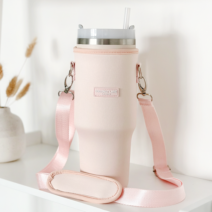 Marshmallow pink tumbler carry case with straw and strap by Cocopup London on a white shelf next to a vase.