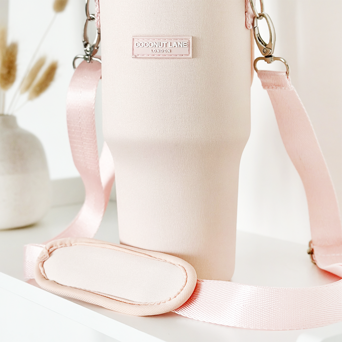 Marshmallow pink tumbler carry case with cross-body strap on a white surface.