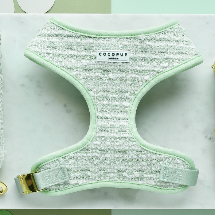 Green textured tweed adjustable neck harness with gold hardware, displayed on a white marble surface.